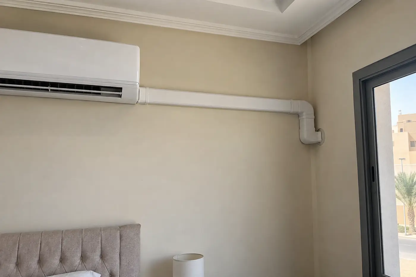 غطاء بلاستيكي أبيض لمسار نحاس مكيف سبليت يمتد على جدار غرفة داخلية حتى الجدار الخارجي