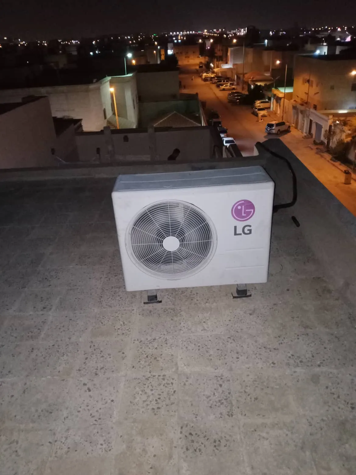 وحدة تكييف خارجية على سطح منزل ليلًا مع إطلالة على الشارع